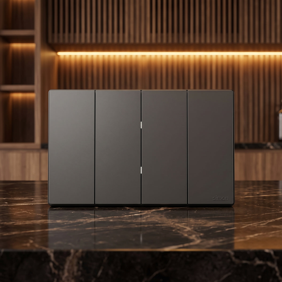 A four-panel dark gray smart wall switch panel with slim vertical handles, displayed on a polished black marble countertop in a modern kitchen setting with warm wood slat backsplash and under-cabinet lighting.